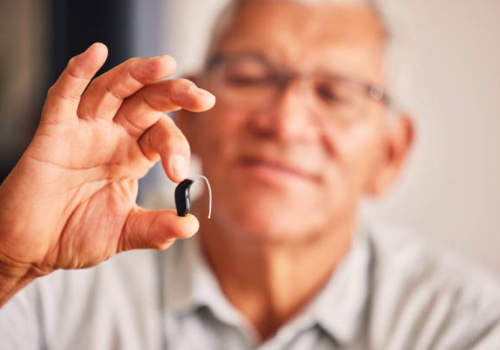 IMG_5148 Hand holding hearing aid, senior man and tech for ears, health and wellness for retirement in nursing home. Elderly person with disability, audio or sound technology to listen in closeup at house