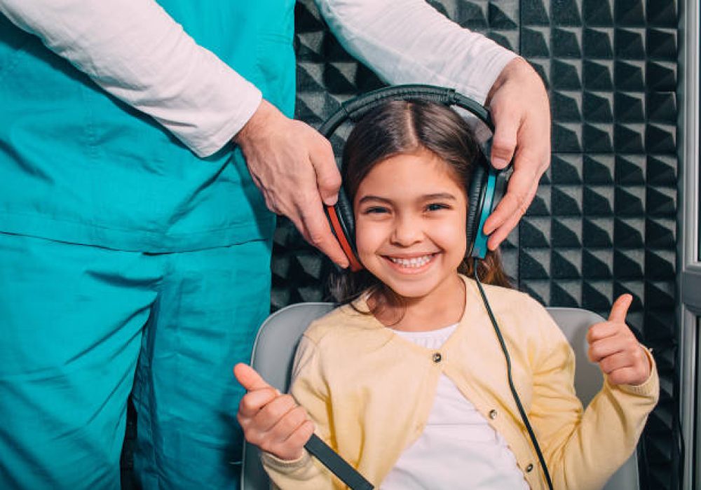 IMG_5161 Positive little mixed race child wearing headphones showing thumbs up while hearing exam.audiometry test